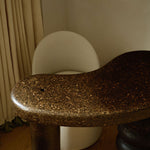 Sculptural MAIE desk in Espresso cork with a satin finish, organically curved tabletop and cylindrical legs.