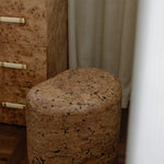 Grain cork side table or stool shown close up beside a wood dresser, highlighting its rounded form and textured surface.