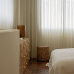 Grain cork side table or stool beside a bed and wood dresser in a softly lit bedroom.