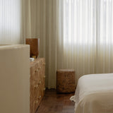 Grain cork side table or stool beside a bed and wood dresser in a softly lit bedroom.
