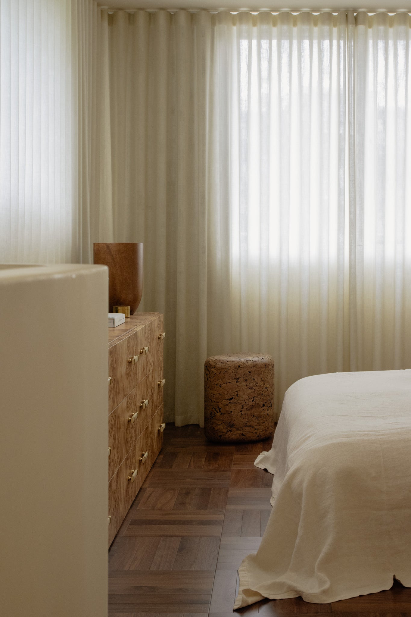 Grain cork side table or stool beside a bed and wood dresser in a softly lit bedroom.