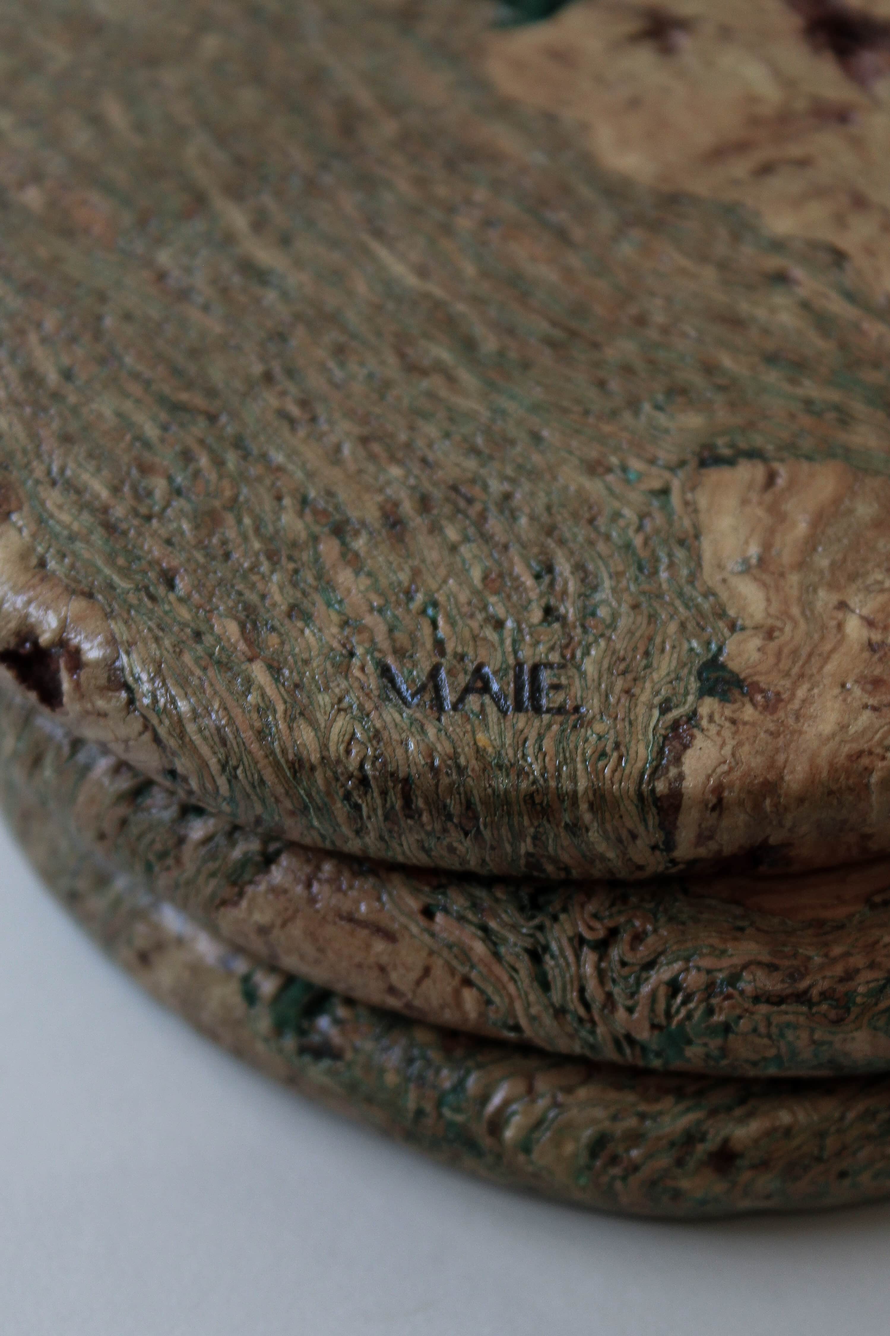 Close-up of the Marbled cork coaster showing soft green lines through warm cork grain, tactile texture and MAIE logo.