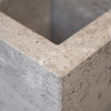 Close-up of a honed Limestone Portland Cube Holder corner, with pale stone, embedded fragments and fine surface pits.