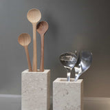 Honed Limestone Portland Cube Holders styled with wooden spoons and metal utensils against a warm grey wall.