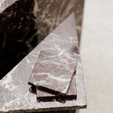 Close-up of Rosso Levanto marble coasters on a matching side table showing fine white veining across a rich burgundy-red surface.