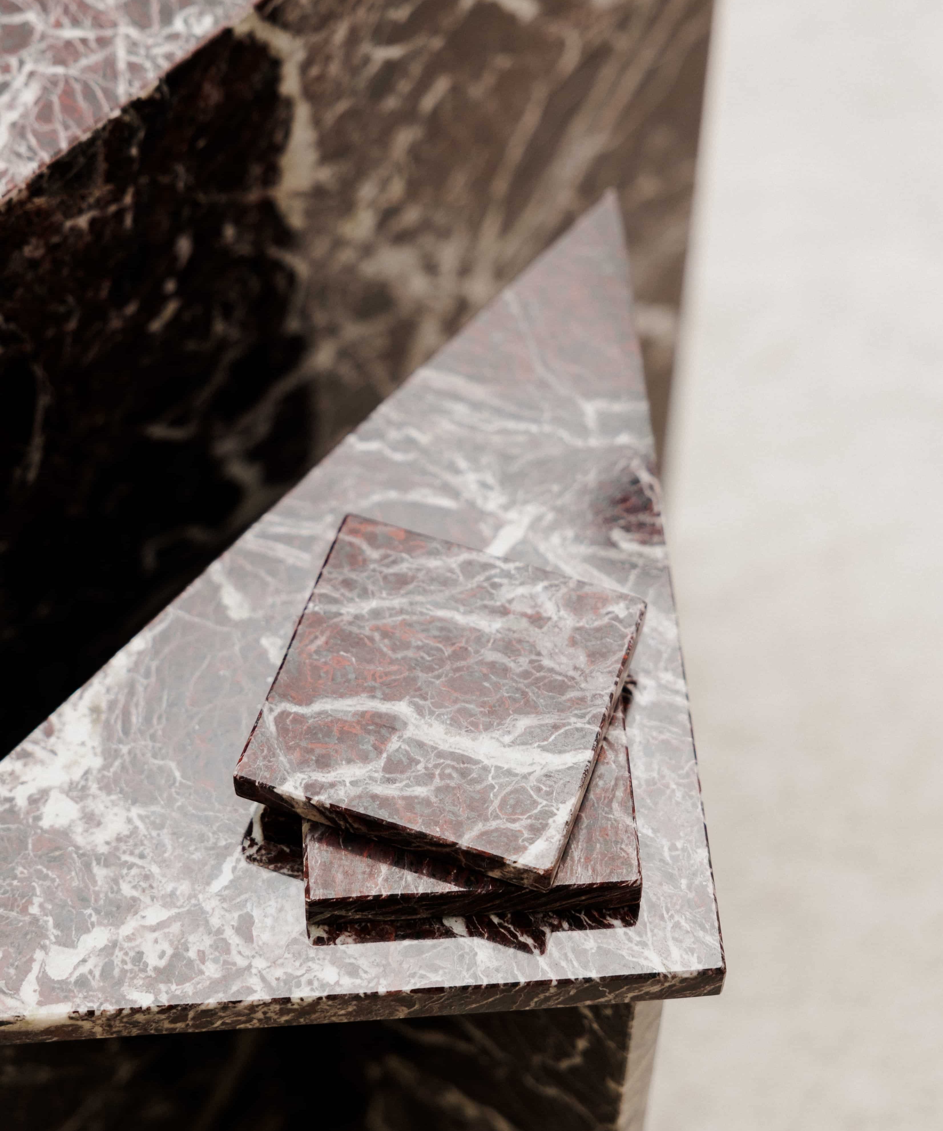 Close-up of Rosso Levanto marble coasters on a matching side table showing fine white veining across a rich burgundy-red surface.