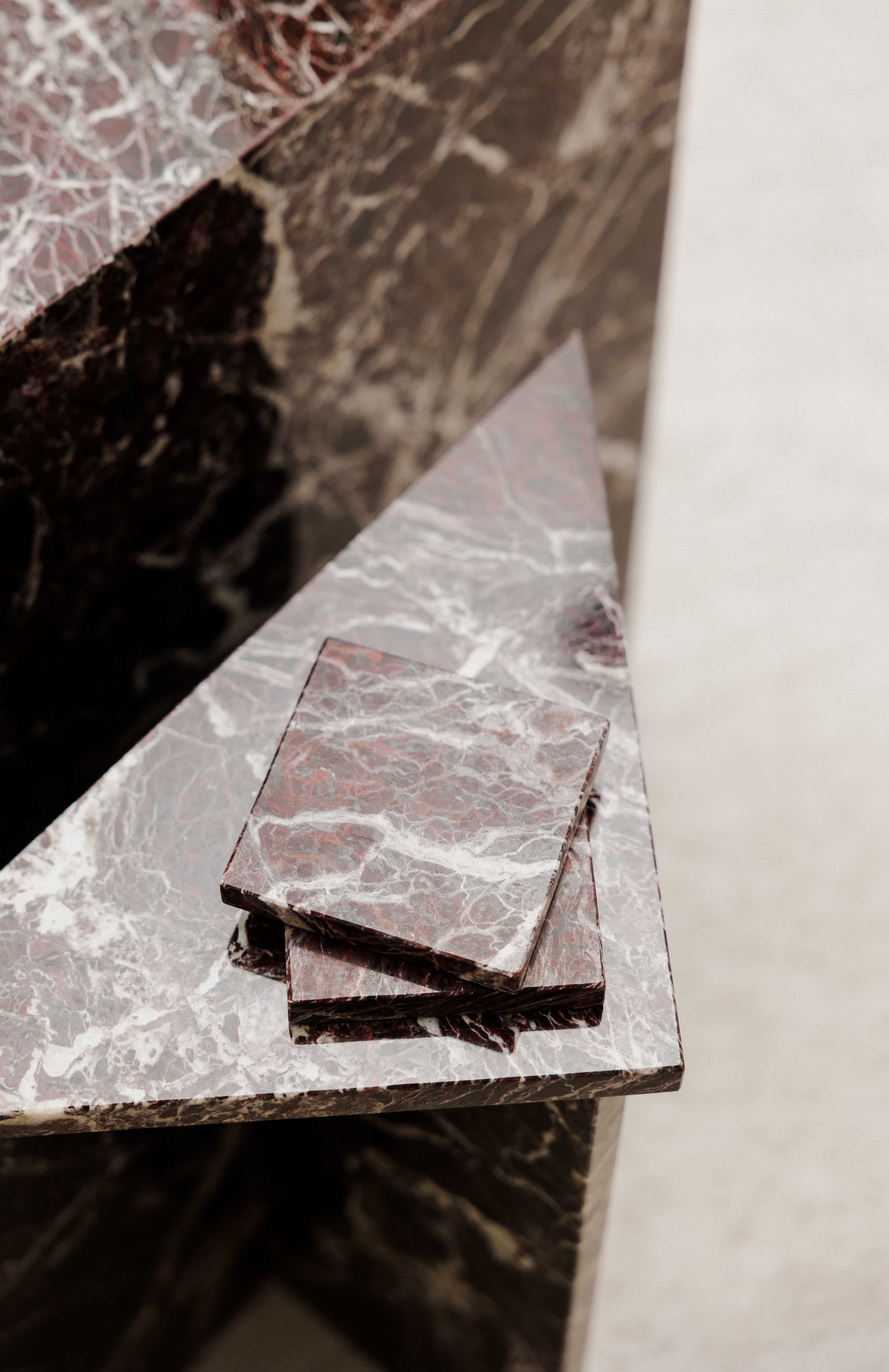Close-up of Rosso Levanto marble coasters on a matching side table showing fine white veining across a rich burgundy-red surface.
