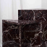 Architectural Rosso Levanto marble side tables with white veining, positioned between grey lounge chairs in a contemporary interior.