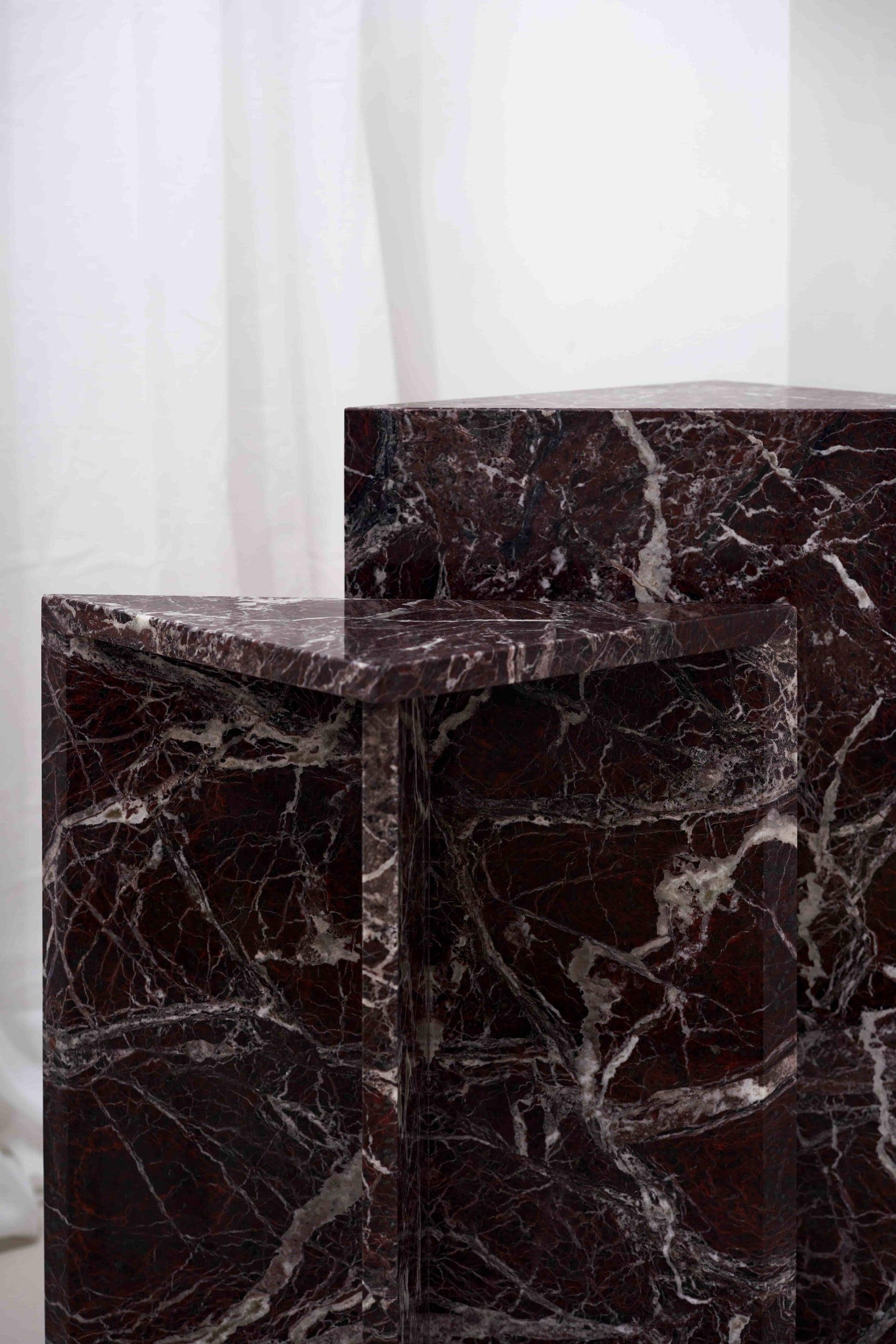Architectural Rosso Levanto marble side tables with white veining, positioned between grey lounge chairs in a contemporary interior.
