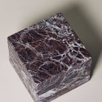 Stack of square MAIE coasters in Rosso Levanto, showing fine white veining across a rich burgundy-red surface.