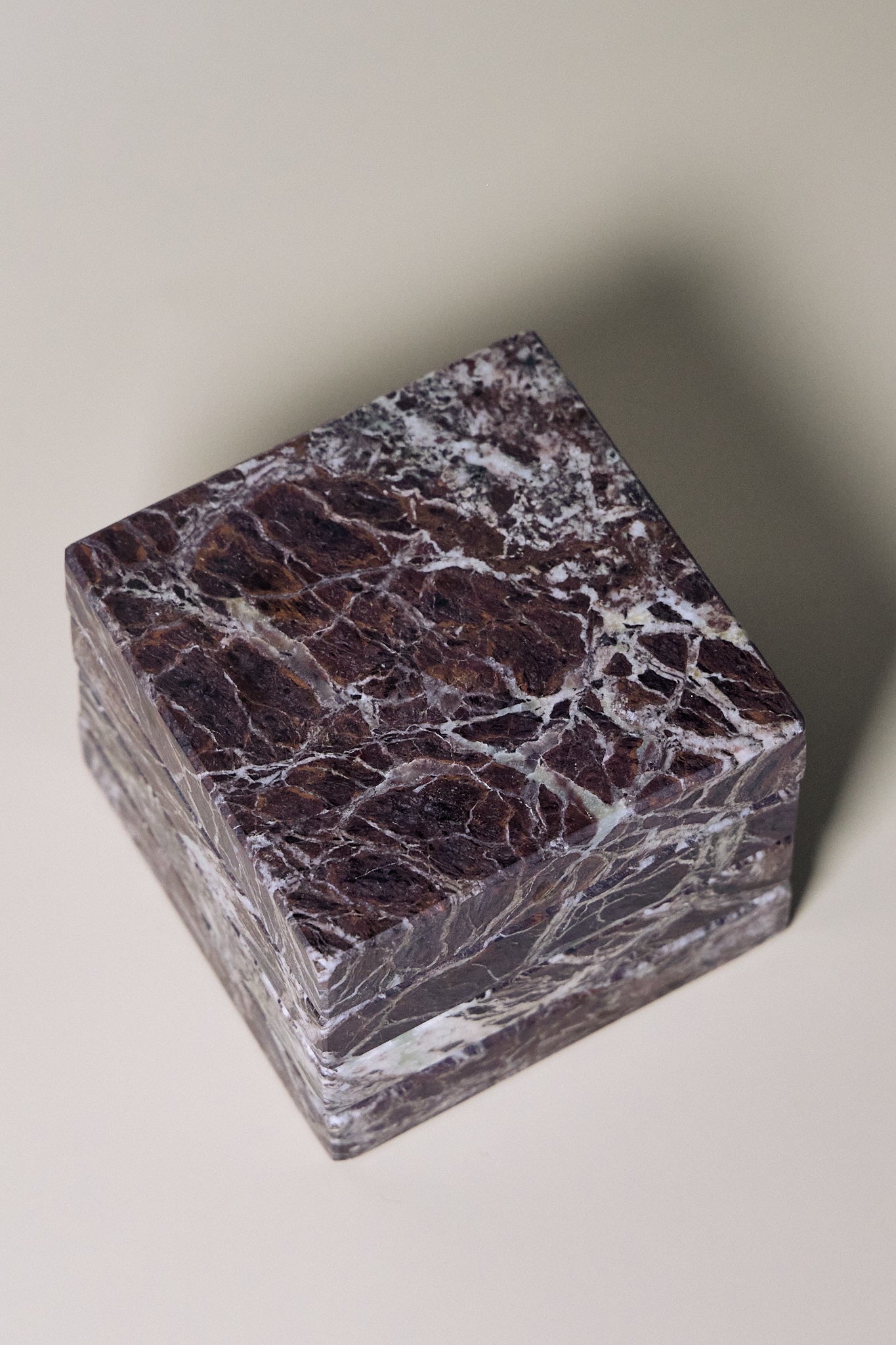 Stack of square MAIE coasters in Rosso Levanto, showing fine white veining across a rich burgundy-red surface.