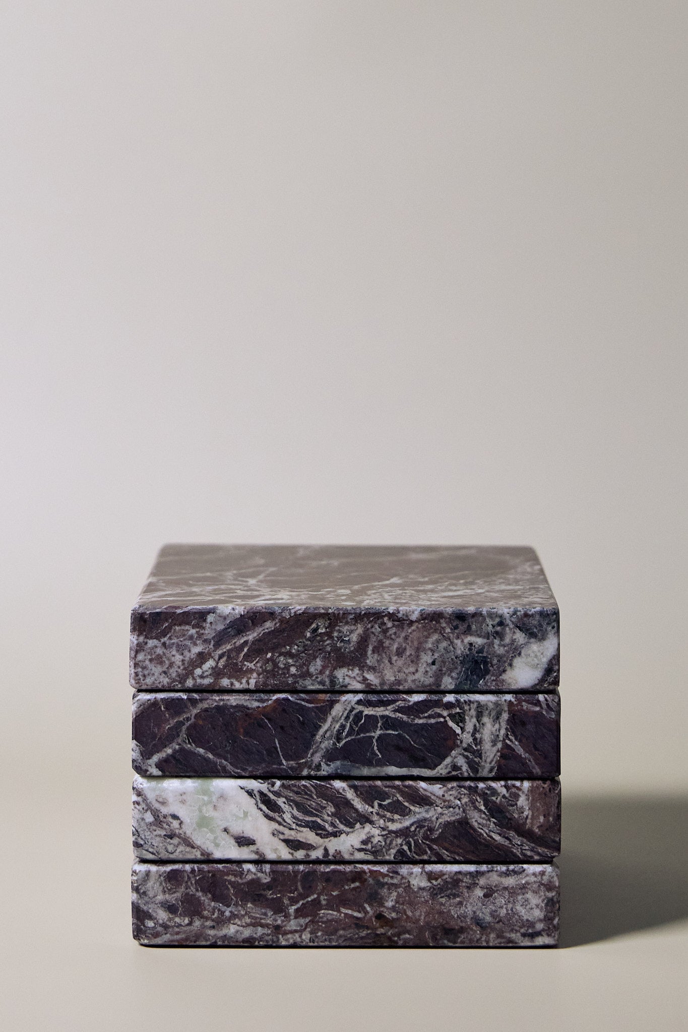 Stack of square MAIE coasters in Rosso Levanto, showing fine white veining across a rich burgundy-red surface.