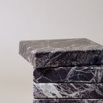 Stack of square MAIE coasters in Rosso Levanto, showing fine white veining across a rich burgundy-red surface.