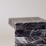 Stack of square MAIE coasters in Rosso Levanto, showing fine white veining across a rich burgundy-red surface.