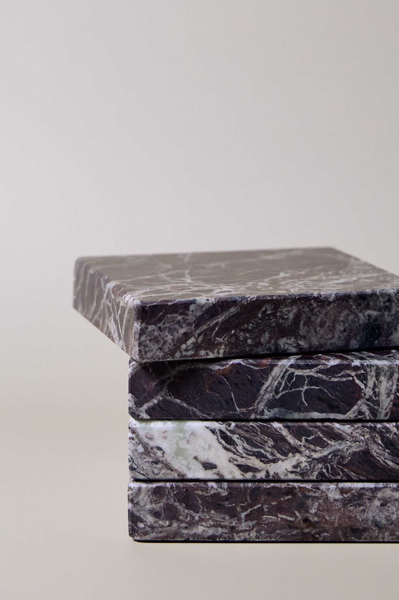 Stack of square MAIE coasters in Rosso Levanto, showing fine white veining across a rich burgundy-red surface.