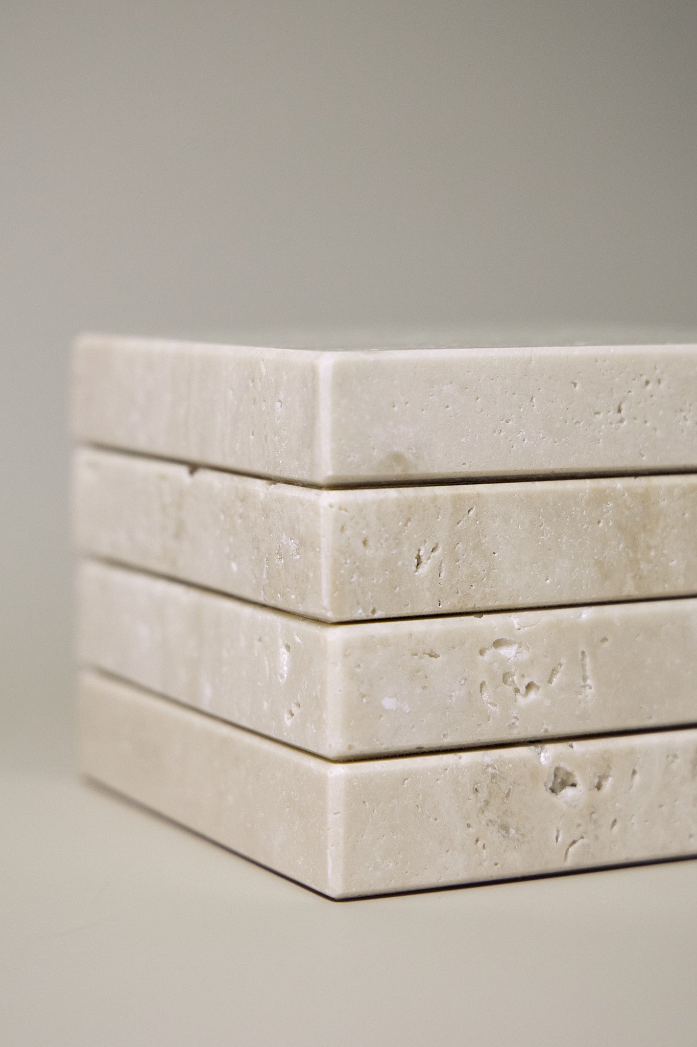 Stack of square MAIE coasters in Travertino Classico VC, showing beige veining, natural pores and tonal variation.