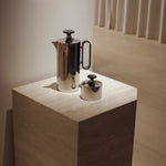 Angular Travertino Classico VC marble plinth with warm-toned veining, styled with a chrome tea set against in a soft contemporary interior.