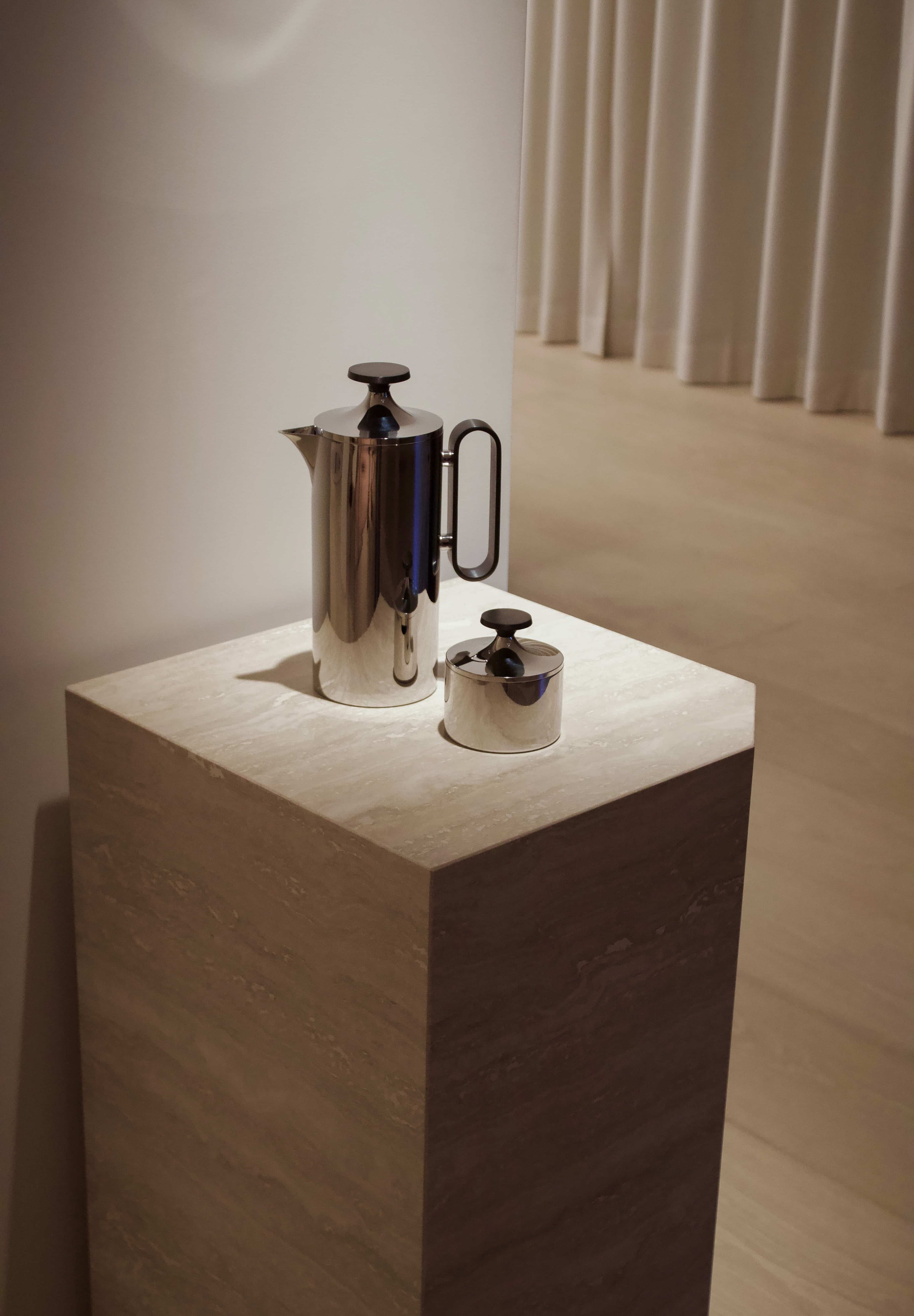 Angular Travertino Classico VC marble plinth with warm-toned veining, styled with a chrome tea set against in a soft contemporary interior.