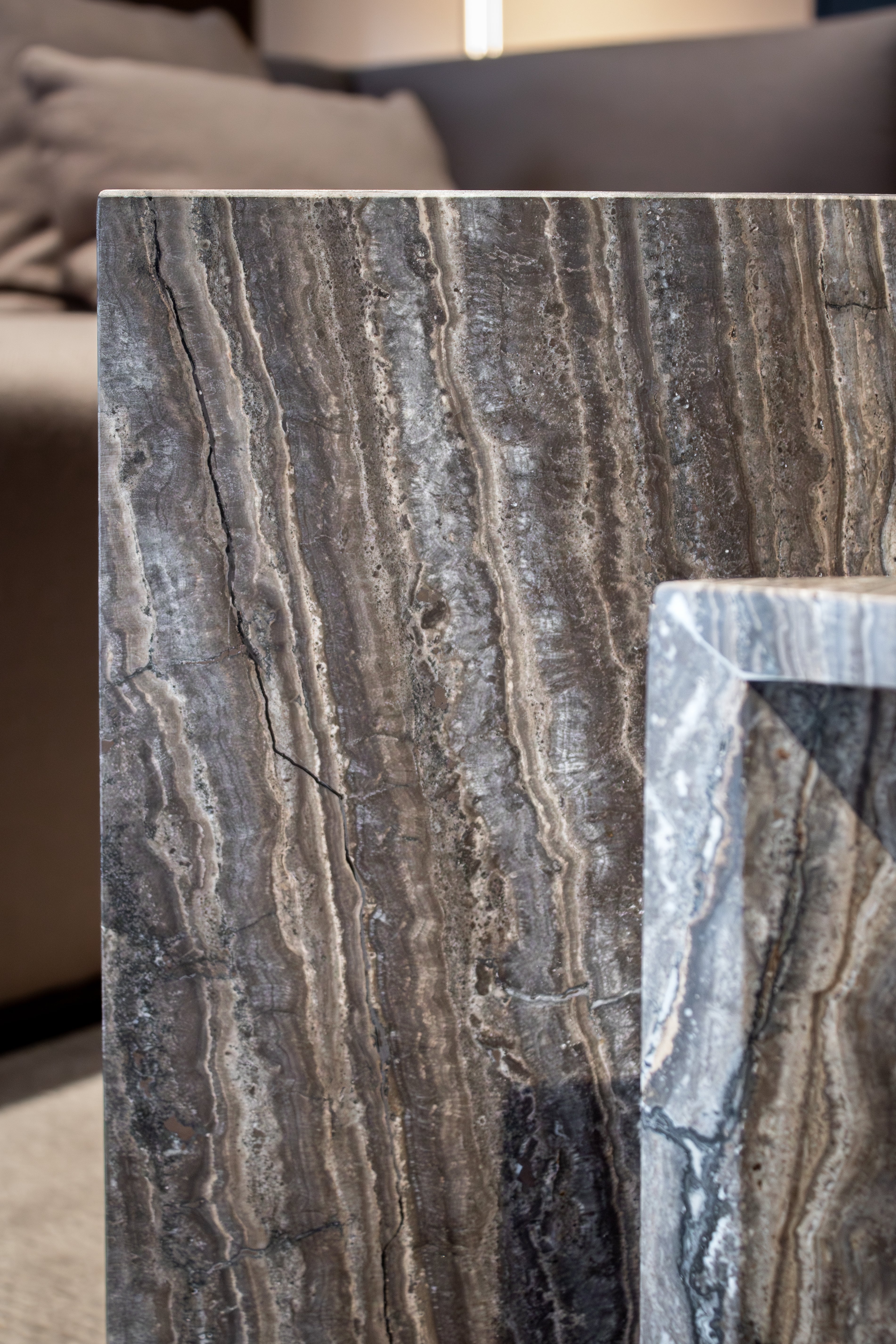 Close-up of Travertino Marrone showing natural pores, irregular veining and layered grey-brown tones along stacked stone edges.