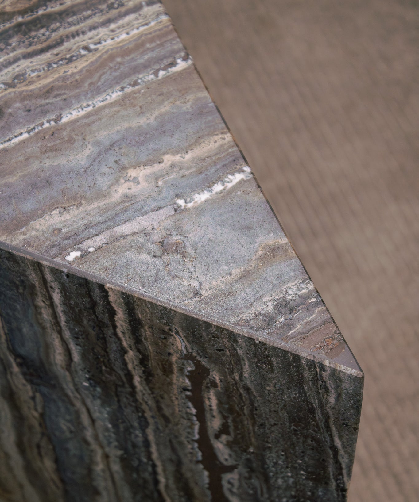 Close-up of Travertino Marrone showing natural pores, irregular veining and layered grey-brown tones along stacked stone edges.