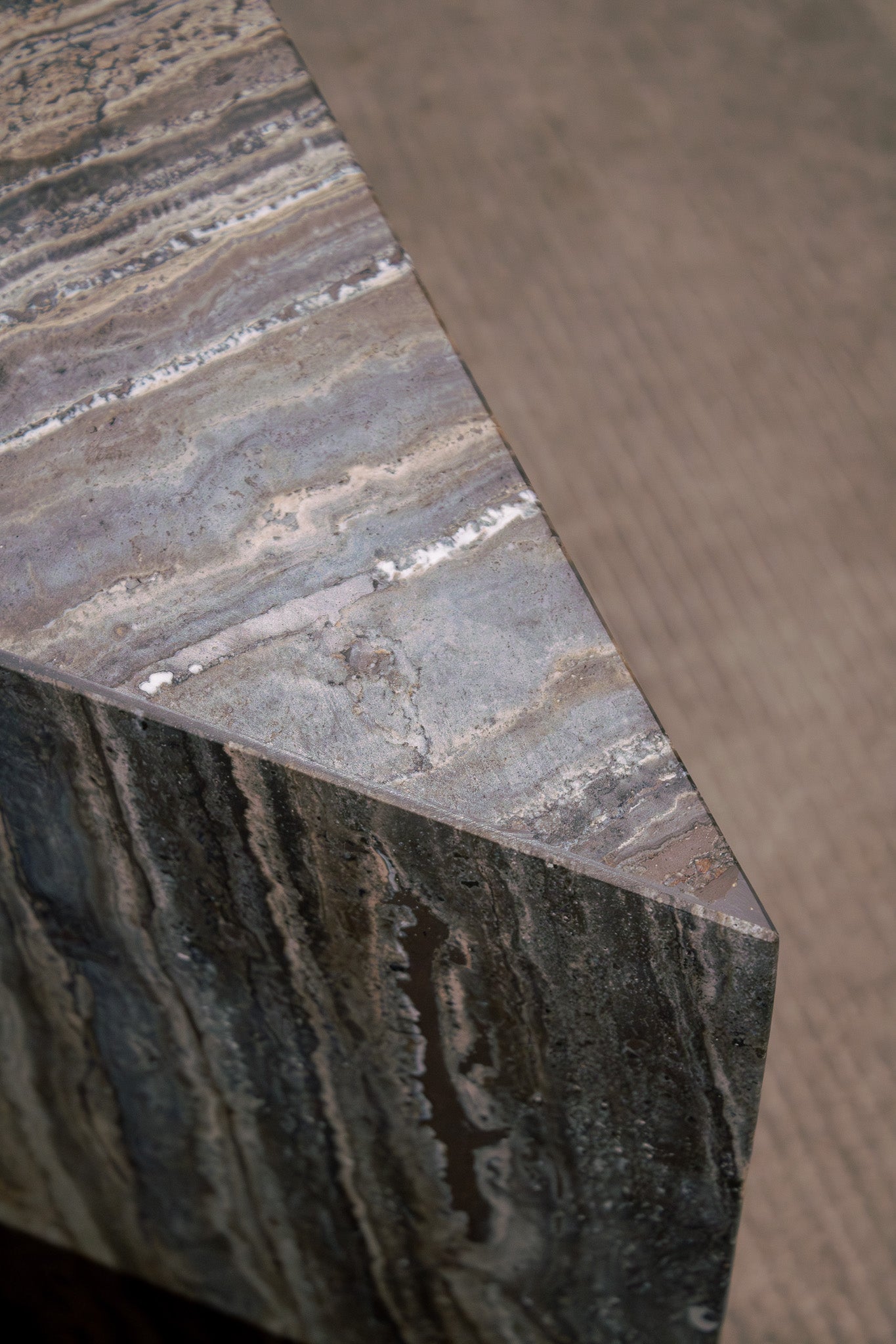 Close-up of Travertino Marrone showing natural pores, irregular veining and layered grey-brown tones along stacked stone edges.