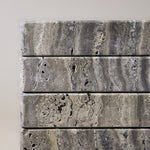 Close-up of Travertino Marrone showing natural pores, irregular veining and layered grey-brown tones along stacked stone edges.