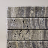 Close-up of Travertino Marrone showing natural pores, irregular veining and layered grey-brown tones along stacked stone edges.