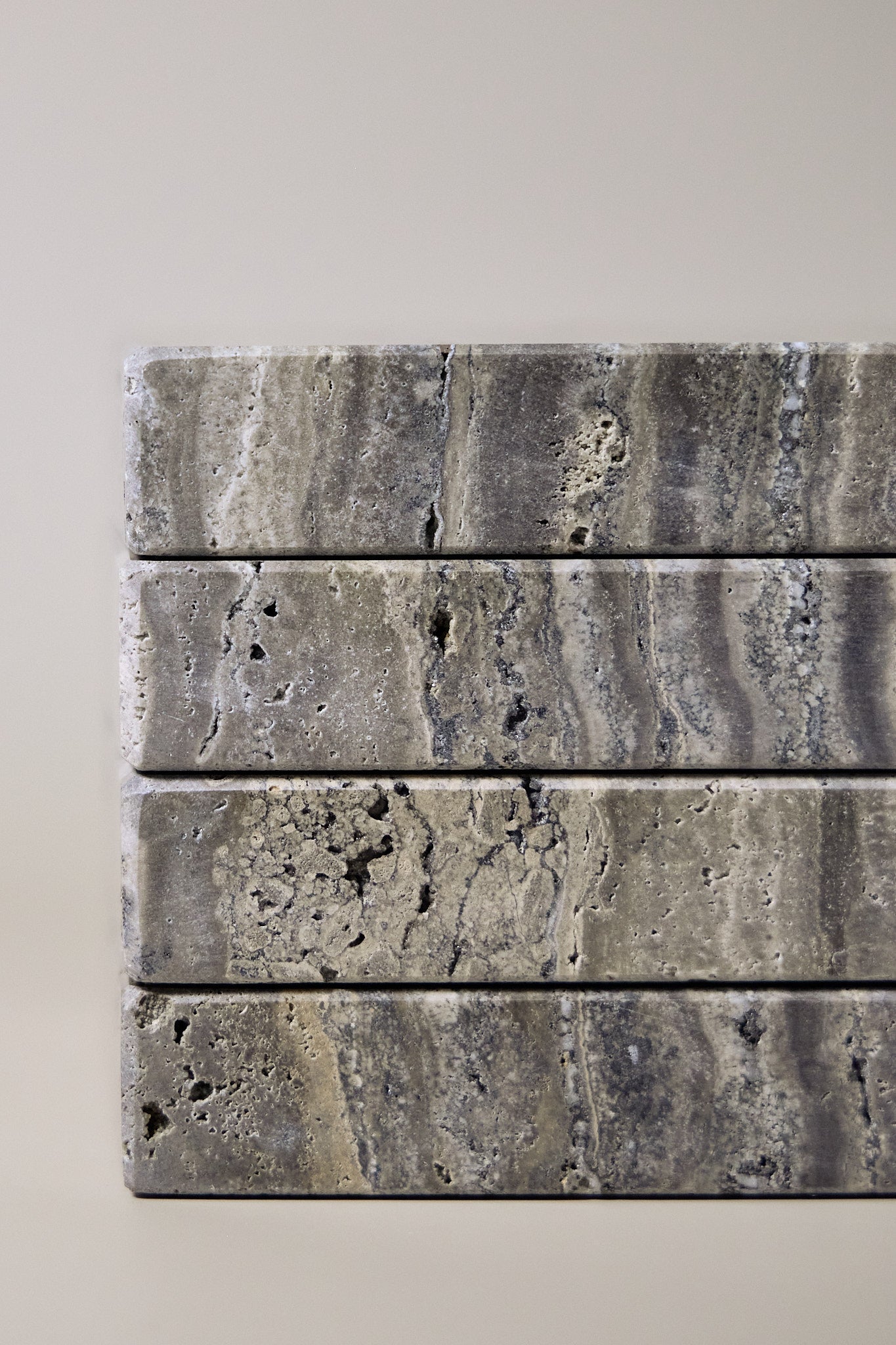 Close-up of Travertino Marrone showing natural pores, irregular veining and layered grey-brown tones along stacked stone edges.