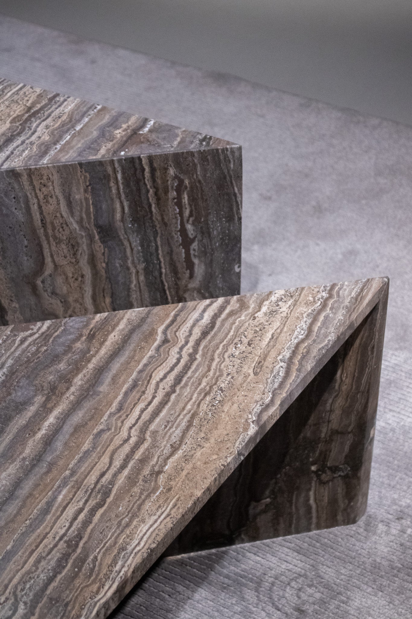 Close-up of Travertino Marrone showing natural pores, irregular veining and layered grey-brown tones along stacked stone edges.