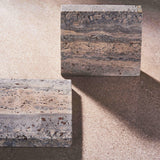 MAIE square coasters in Travertino Marrone, showing layered grey-brown veining, natural pores and straight edges.