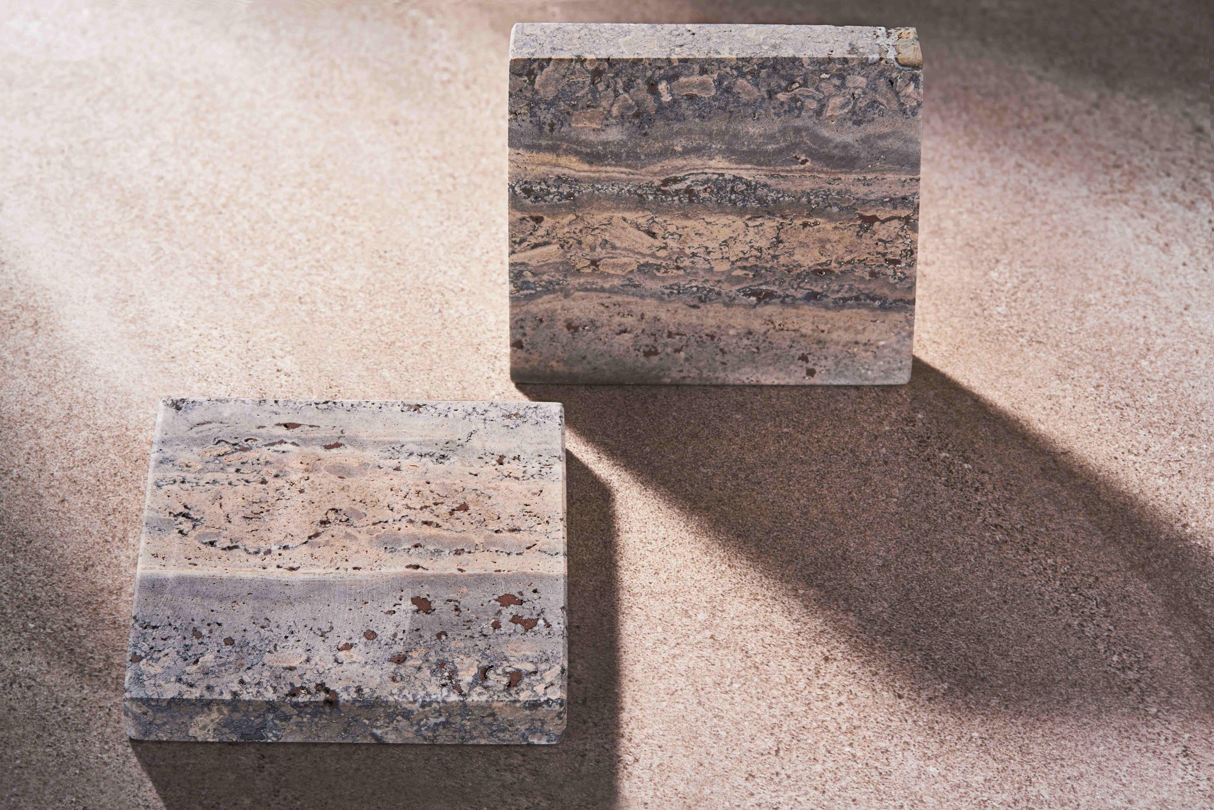 MAIE square coasters in Travertino Marrone, showing layered grey-brown veining, natural pores and straight edges.