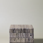 Stack of square MAIE coasters in Travertino Marrone, showing layered grey-brown veining, natural pores and straight edges.