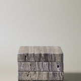 Stack of square MAIE coasters in Travertino Marrone, showing layered grey-brown veining, natural pores and straight edges.
