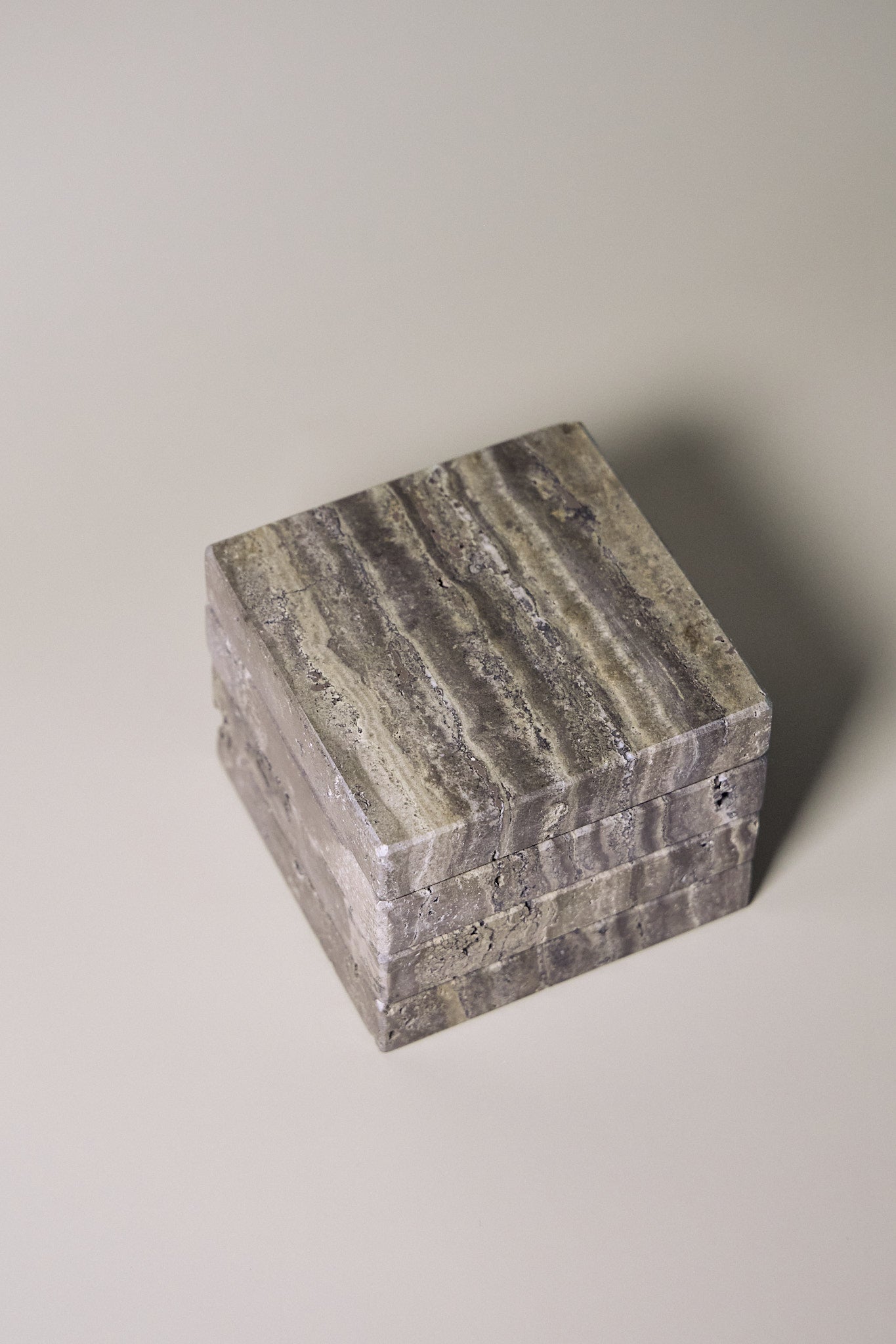 Stack of square MAIE coasters in Travertino Marrone, showing layered grey-brown veining, natural pores and straight edges.