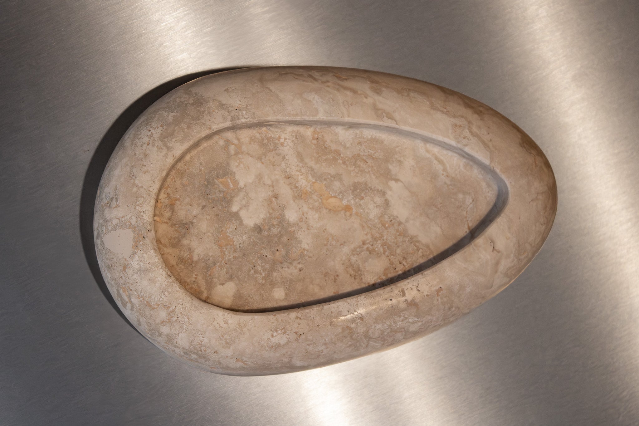 Egg-shaped Travertino Classico CC marble bowl with warm-toned veining on a stainless steel surface.